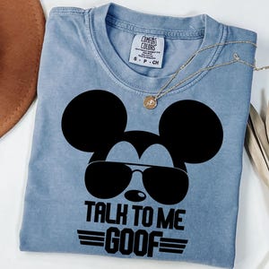 Puede incluir: Una camiseta azul claro de cuello redondo con un gr&aacute;fico negro de la silueta de un rat&oacute;n con gafas de sol. El texto debajo del gr&aacute;fico dice TALK TO ME GOOF con l&iacute;neas horizontales a los lados. Incluye la etiqueta de marca Comfort Colors.