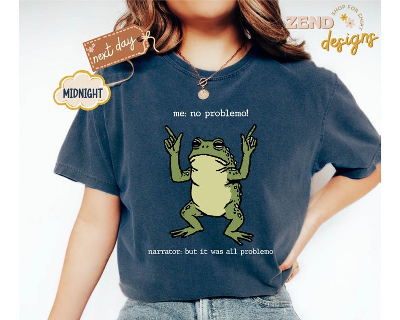 Puede incluir: Camiseta azul marino con una ilustraci&oacute;n de rana verde y el texto "me: no problemo!" y "narrator: but it was all problemo". La camiseta tiene un corte relajado, ideal para uso diario.