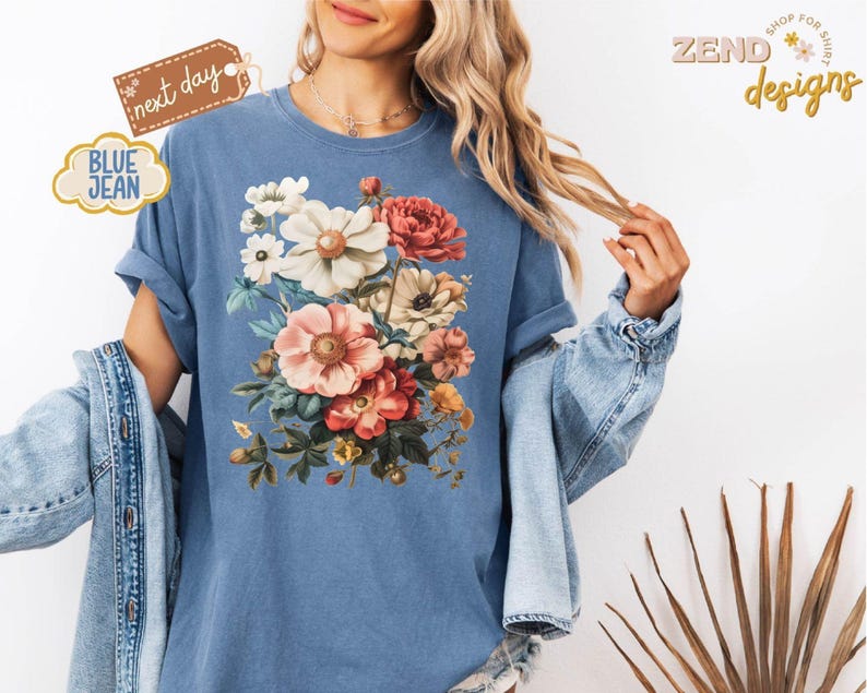 Puede incluir: Camiseta azul vaquera con un dise&ntilde;o de ramo de flores en tonos rosas, rojos, blancos y amarillos. La camiseta tiene las mangas enrolladas y se ven las palabras "next day" y "blue jean".