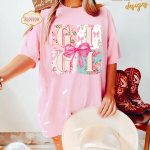 Puede incluir: Camiseta rosa con un dise&ntilde;o floral y la palabra "Gigi" en estilo patchwork. La camiseta tiene un corte holgado y es perfecta para el uso diario.