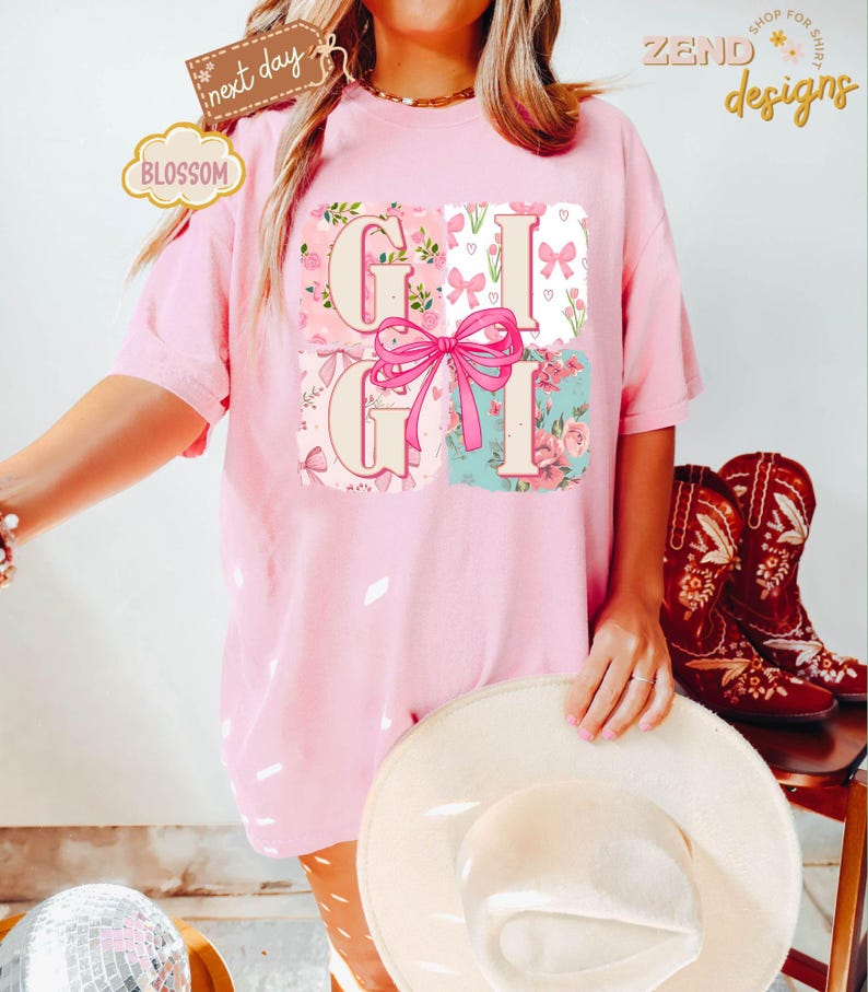 Puede incluir: Camiseta rosa con un dise&ntilde;o floral y la palabra "Gigi" en estilo patchwork. La camiseta tiene un corte holgado y es perfecta para el uso diario.