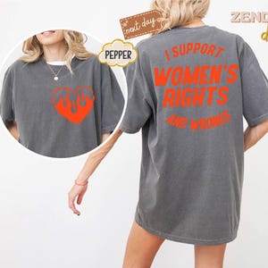 May include: A gray t-shirt with the text "I support women's rights and wrongs" printed in orange on the back. The front of the shirt features a red heart with flames.