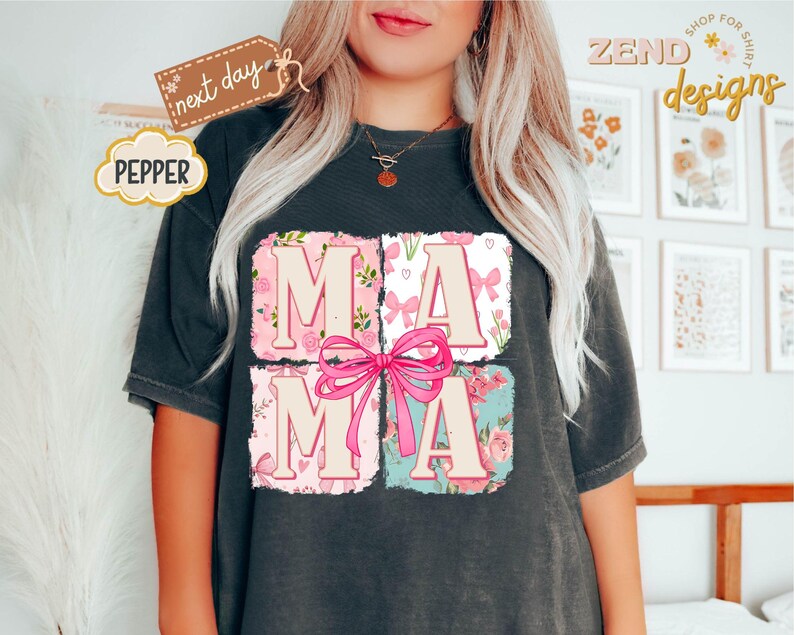 Puede incluir: Una camiseta negra con un dise&ntilde;o gr&aacute;fico de la palabra "MAMA" en letras rosas y blancas rodeada de dise&ntilde;os florales y de lazos.