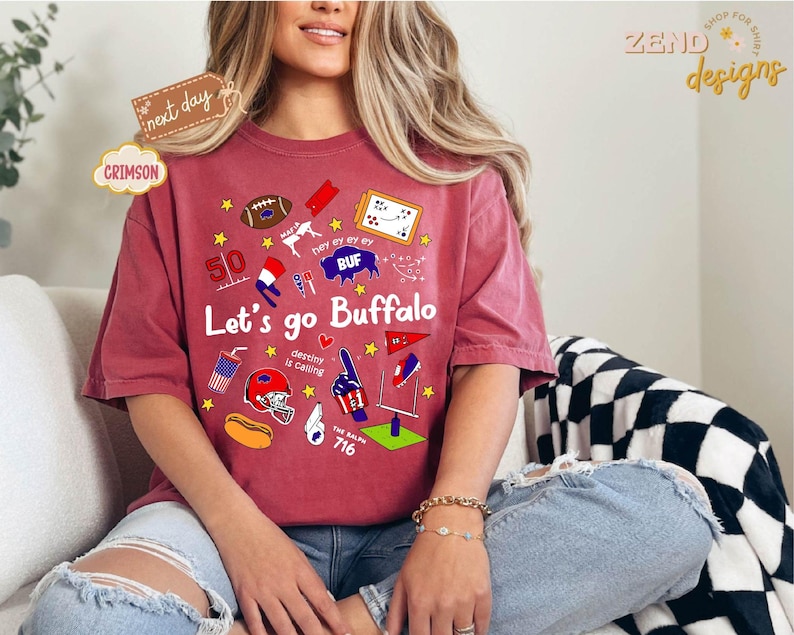 May include: Crimson-colored t-shirt with the text "Let's go Buffalo" and various graphics, including a football, stars, and a helmet. The shirt also features the text "destiny is calling" and the number "716".