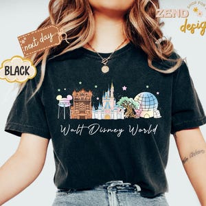May include: Black t-shirt featuring a colorful illustration of Walt Disney World landmarks, including Cinderella Castle and Spaceship Earth. The words "Walt Disney World" are written below the graphic. A tag reads "next day".