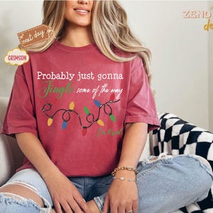 Pode incluir: Camiseta vermelha carmesim com o texto "Probably just gonna Jingle some of the way" e uma sequ&ecirc;ncia de luzes de Natal. A camisa tamb&eacute;m tem o texto "I'm tired". A camisa faz parte da cole&ccedil;&atilde;o "Zend Designs".