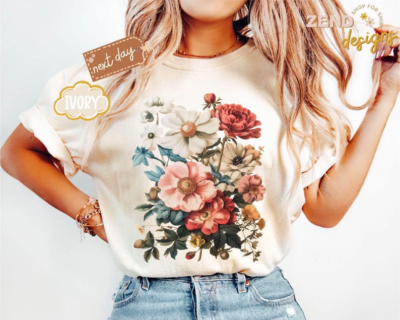 Puede incluir: Camiseta de color marfil con un dise&ntilde;o de ramo floral en tonos rosa, rojo, blanco y azul. La camiseta tiene mangas cortas y cuello redondo. Las palabras "next day" y "IVORY" est&aacute;n impresas en la camiseta.