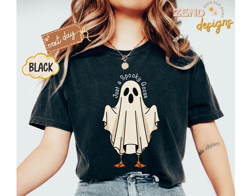May include: Black t-shirt featuring a cartoon ghost with the text "Just a Spooky Goose". The ghost has a white body, black eyes, and orange feet. The shirt also has a "next day" tag and the word "BLACK".
