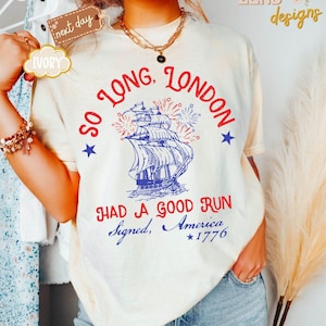 May include: Cream-coloured t-shirt featuring the text "So Long, London" above a blue and white ship illustration, with fireworks and stars. The text "Had a Good Run, Signed, America, 1776" is below the ship.