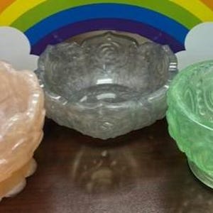 May include: Three decorative bowls with intricate designs. The bowls are made of clear glass with a frosted finish. The bowls are in shades of pink, grey, and green.