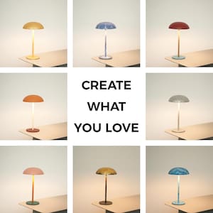 Può includere: Una collezione di piccole lampade da tavolo moderne con paralumi a forma di fungo in vari colori, tra cui giallo, blu, rosso e rosa. Ogni lampada ha uno stelo sottile e una base circolare. Il testo "CREATE WHAT YOU LOVE" è al centro.