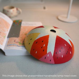 Può includere: Paralume per lampada artigianale non assemblato con un design geometrico colorato in rosso, arancione, giallo, rosa e bianco. Il design ricorda una anguria.