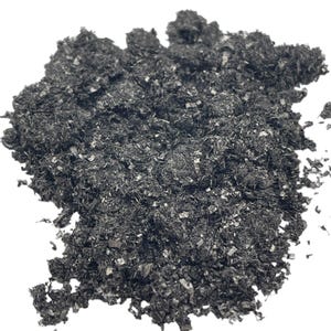 May include: A close-up of a pile of black graphite flakes. The flakes are small and irregular in shape, and they have a metallic sheen.