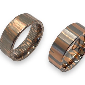 May include: Two matching wedding bands with a unique hammered finish. The bands are made of a combination of silver and copper, creating a striped pattern.