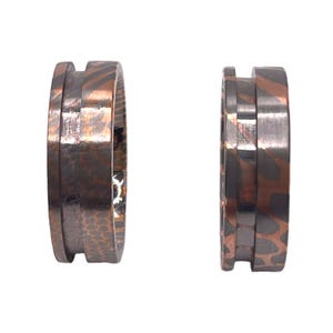 May include: Two copper and black patterned rings with a hammered texture. The rings are stacked on top of each other.