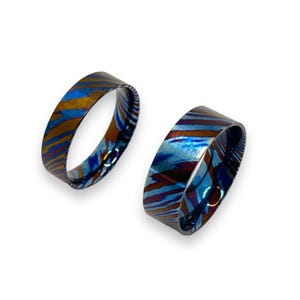 May include: Two blue and orange patterned metal rings. The rings are wide and have a beveled edge.