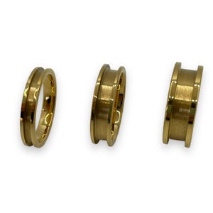May include: Three gold-coloured metal rings of different sizes. The rings are all smooth and have a slightly rounded edge.