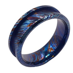 May include: A blue, purple and orange patterned metal ring. The ring is wide and has a bevelled edge.