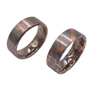 May include: Two matching wedding bands with a unique, textured, animal print design. The bands are made of a combination of silver and rose gold.
