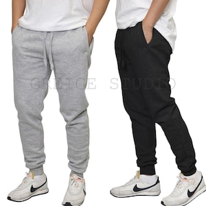 May include: Two pairs of sweatpants, one light gray and one black, are displayed. Both have a drawstring waist and cuffed ankles. The text "GRICE STUDIO" is visible on the pants. The sweatpants are paired with white sneakers.