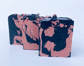 May include: Three bars of handmade soap with a marbled design in shades of black and pink.