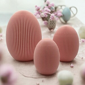 Può includere: Tre uova di Pasqua rosa con una texture a coste. Le uova sono disposte a forma di piramide, con l'uovo più grande in basso e quello più piccolo in alto.