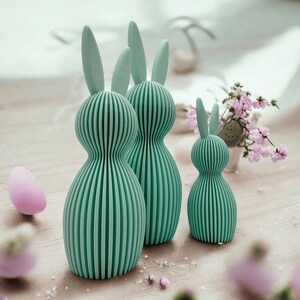 Può includere: Tre statuine di coniglio blu turchese con una texture a coste. I conigli sono di dimensioni diverse e sono disposti in fila dal più grande al più piccolo.