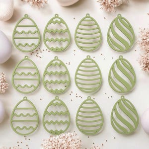 Può includere: Dodici ornamenti per uova di Pasqua in legno verde con diversi disegni ritagliati. I disegni includono strisce, onde e zig zag.