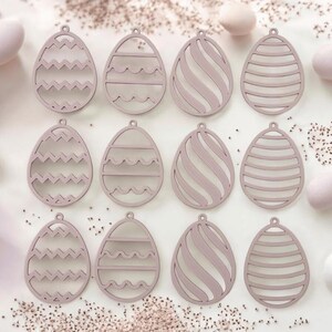 Può includere: Dodici ornamenti per uova di Pasqua in legno rosa con diversi disegni ritagliati. I disegni includono zig zag, onde e spirali.