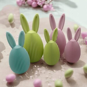 Può includere: Cinque decorazioni a forma di coniglio pasquale realizzate in materiale testurizzato. I conigli sono in tonalità di verde e rosa.