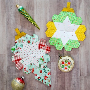 May include: Two handmade Christmas decorations in the shape of a star and a tree. The decorations are made from fabric scraps in a variety of colours and patterns, including red, green, white, and yellow. The decorations are hanging from a gold string.