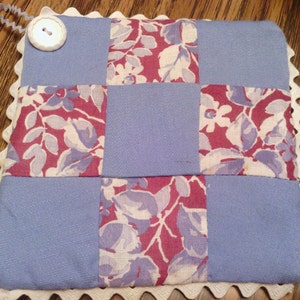 May include: A blue and red patchwork pot holder with a white scalloped edge and a white button.