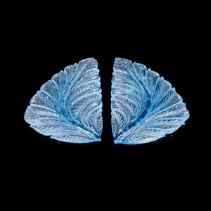 Könnte beinhalten: Ein Paar hellblaue, durchscheinende Edelsteine, die in Form symmetrischer Blätter geschnitzt sind. Jedes Stück weist komplizierte, detaillierte Adernmuster auf, die in die Oberfläche eingraviert sind und ein strukturiertes Aussehen mit poliertem Finish erzeugen.