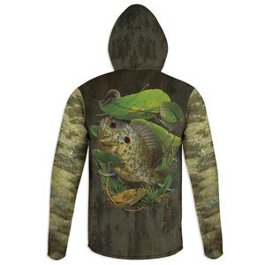 May include: A green and brown long-sleeved hoodie with a camouflage pattern. The back of the hoodie features a realistic image of a green and brown fish swimming in a pond with lily pads.