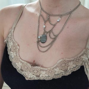 May include: A layered silver chain necklace with a grey stone pendant and white beads.