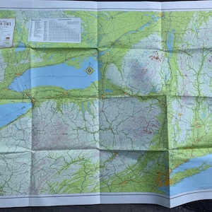 Puede incluir: Un mapa vintage del estado de Nueva York con redes de carreteras detalladas, ciudades y características geográficas. El mapa está impreso en un fondo blanco con colores verde, azul y marrón.
