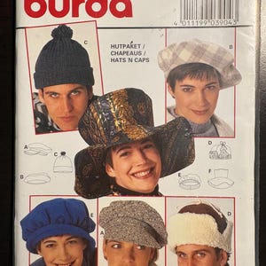 May include: A Burda sewing pattern envelope 3904 for various hats and caps. The cover displays six different headwear styles including a dark blue pom-pom beanie, a plaid beret, a wide-brimmed patterned hat, a blue cap, a tweed cap, and a faux fur trapper hat.