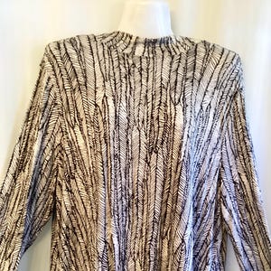 May include: A long-sleeved shirt with a white background and a black feather pattern.