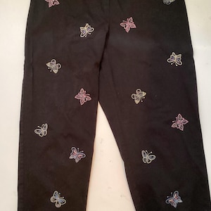 May include: Black pants with embroidered butterfly designs in pink, blue, and yellow. The pants have a straight leg cut and a high waist. A casual style for everyday wear.