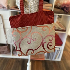 May include: A red corduroy tote bag with a beige fabric lining featuring a swirl pattern in shades of orange and pink.