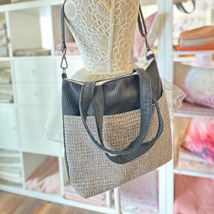 May include: A gray and beige tote bag with a corduroy top and a woven bottom. The bag has two long straps and a zipper closure.