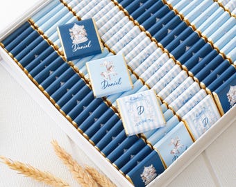 May include: A white box filled with rows of rectangular chocolate bars wrapped in blue and light blue striped paper. Some bars feature a carousel horse illustration and the name Daniel, while others display a decorative letter D in blue.