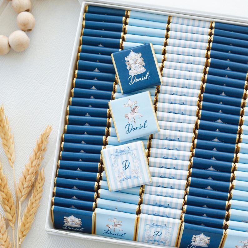 May include: A box of personalized chocolates in shades of blue. The chocolates are arranged in rows and feature designs with the name "Daniel" and the letter "D". Some chocolates have carousel and horse illustrations.