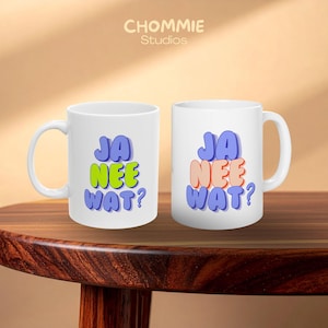 May include: Two white ceramic mugs featuring the text JA NEE WAT? in a bold, rounded font. The left mug displays the word NEE in bright lime green, while the right mug displays the word NEE in a soft peach colour. Both mugs have blue lettering.