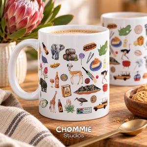 May include: A white ceramic mug featuring a colourful collage of South African icons, including an elephant, giraffe, springbok, Table Mountain, and various food and drink items. A small rectangular label reads Made in South Africa.