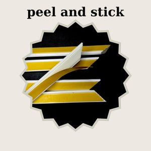 Pode incluir: Tiras de acabamento flex&iacute;veis brancas com um verso adesivo amarelo e uma camada protetora castanha parcialmente removida. O texto peel and stick &eacute; exibido acima das tiras, dispostas sobre um fundo preto dentro de uma forma de estrela.