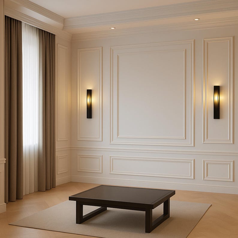 Pode incluir: Uma mesa de centro quadrada e baixa de madeira castanho-escura assenta sobre um tapete claro. A sala apresenta paredes em branco-sujo com molduras decorativas, dois candeeiros de parede pretos verticais com luz quente e cortinas bege.