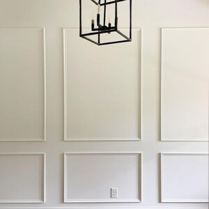 May include: A white wall with decorative moulding. A square, black metal light fixture hangs from the ceiling.