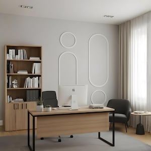 May include: A home office setup featuring a light wood desk with a black metal frame, a silver desktop computer, and a black office chair. A tall matching wood bookcase stands to the left, while a dark gray armchair sits near a small side table.