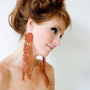 Peut inclure: Une femme aux cheveux roux portant de longues boucles d'oreilles pendantes en dentelle crochetée orange.